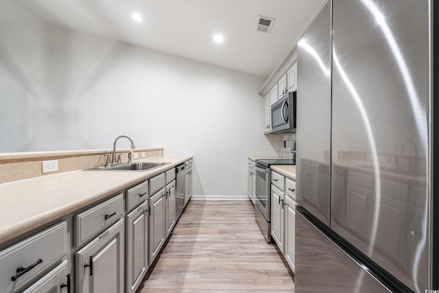 kitchen with stainless steel appliances, gray cabinets, light countertops, light wood-style flooring, and a sink