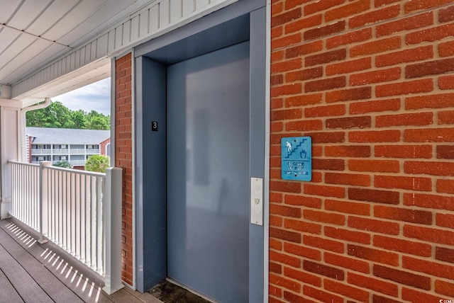 view of exterior entry with a balcony, elevator, and brick siding