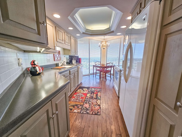 kitchen featuring white appliances, light hardwood / wood-style flooring, a tray ceiling, a notable chandelier, and crown molding