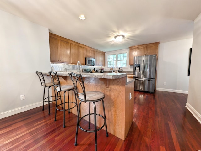 kitchen featuring dark wood-type flooring, appliances with stainless steel finishes, a breakfast bar area, and kitchen peninsula