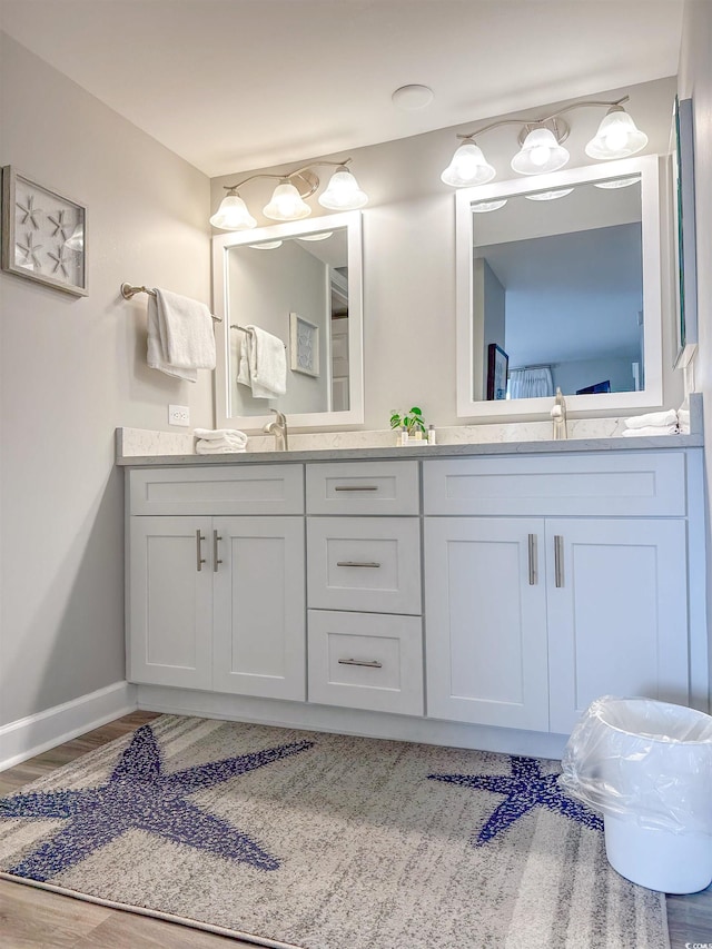 full bathroom featuring baseboards, double vanity, a sink, and wood finished floors