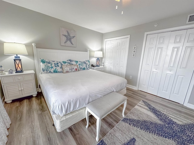 bedroom featuring baseboards, visible vents, wood finished floors, and two closets