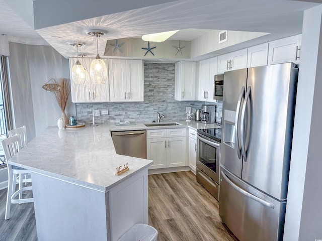 kitchen with light wood-type flooring, tasteful backsplash, stainless steel appliances, kitchen peninsula, and sink