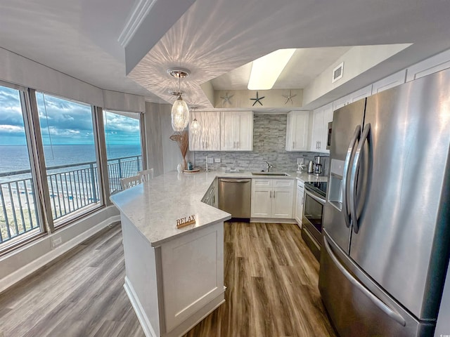 kitchen with appliances with stainless steel finishes, light hardwood / wood-style floors, a water view, kitchen peninsula, and decorative backsplash