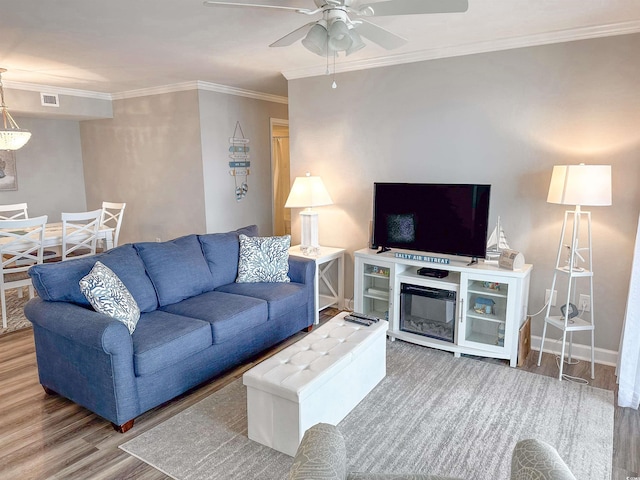 living area with a ceiling fan, ornamental molding, baseboards, and wood finished floors