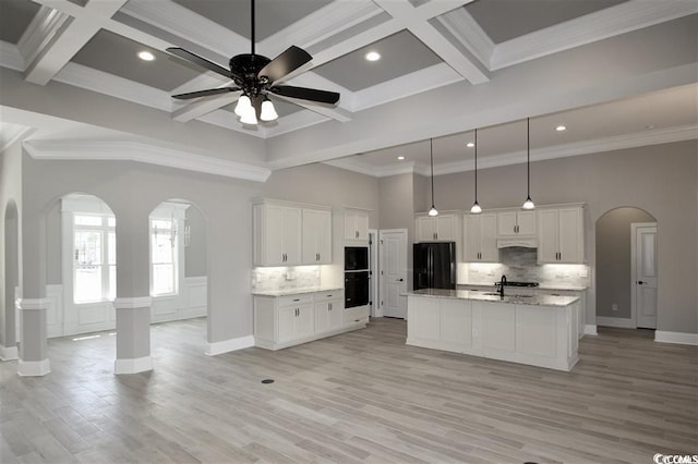 kitchen with coffered ceiling, beamed ceiling, light hardwood / wood-style flooring, black appliances, and a center island with sink