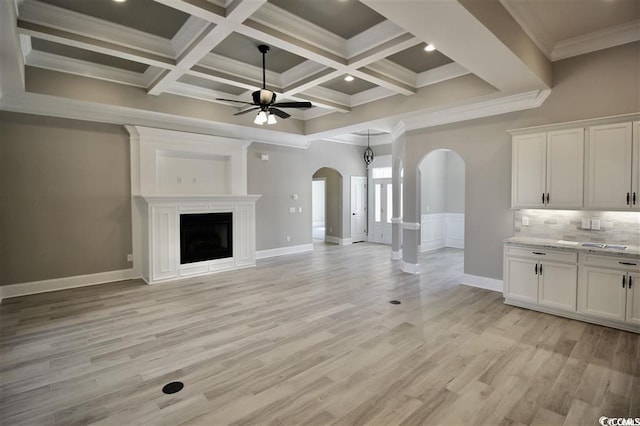 unfurnished living room with coffered ceiling, beamed ceiling, crown molding, light hardwood / wood-style flooring, and ceiling fan