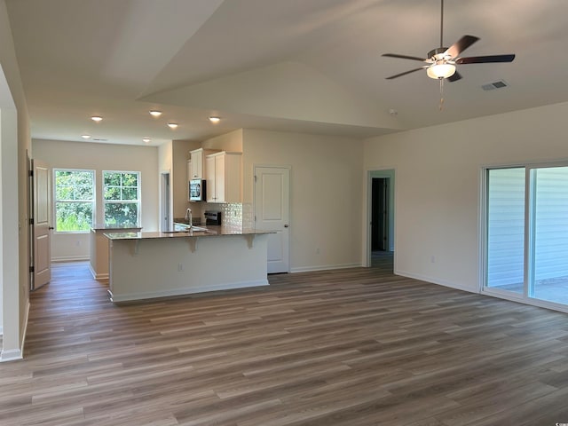 kitchen featuring a kitchen breakfast bar, light hardwood / wood-style floors, vaulted ceiling, white cabinets, and ceiling fan