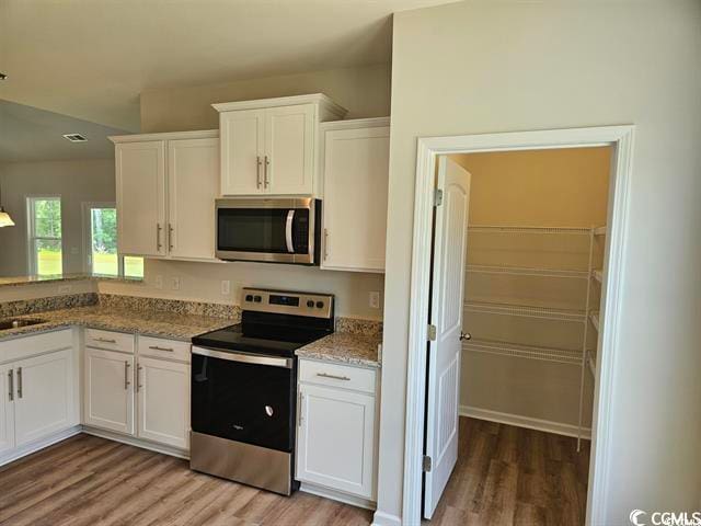 kitchen with white cabinets, light stone countertops, stainless steel appliances, light wood-type flooring, and sink