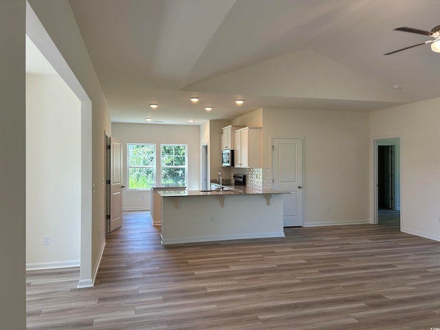 kitchen featuring decorative backsplash, kitchen peninsula, light wood-type flooring, a kitchen bar, and ceiling fan