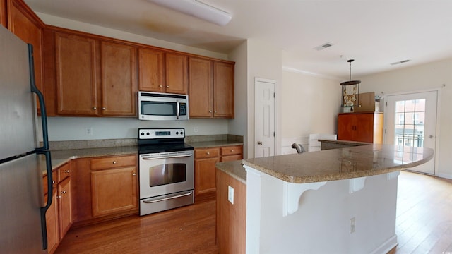 kitchen featuring stainless steel appliances, decorative light fixtures, wood-type flooring, and a kitchen island