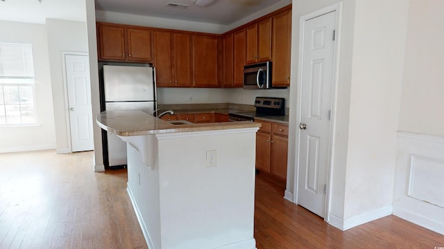 kitchen featuring sink, a breakfast bar area, appliances with stainless steel finishes, light hardwood / wood-style floors, and an island with sink