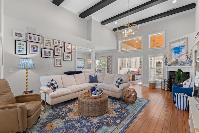 living area featuring beamed ceiling, a glass covered fireplace, a chandelier, a high ceiling, and hardwood / wood-style flooring