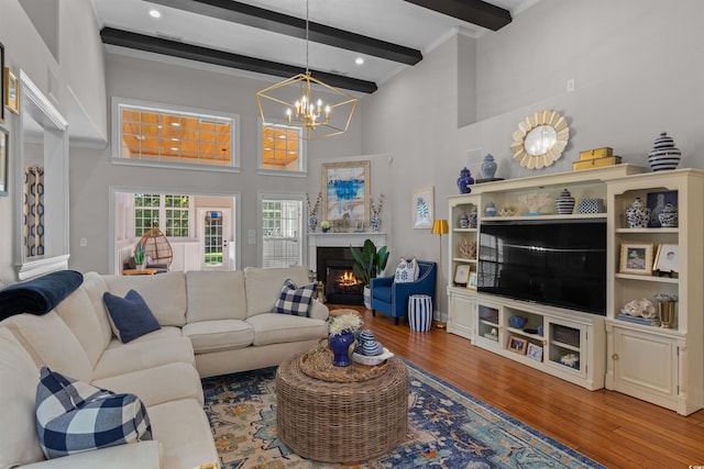 living area with a towering ceiling, a notable chandelier, a lit fireplace, beam ceiling, and hardwood / wood-style flooring