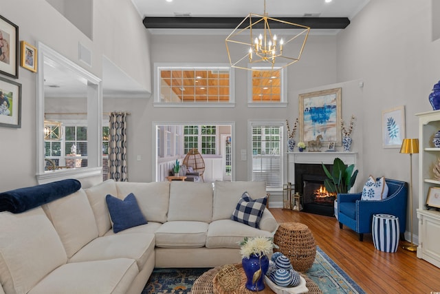 living area with a towering ceiling, ornamental molding, a glass covered fireplace, wood-type flooring, and a notable chandelier