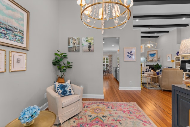 living area featuring baseboards, an inviting chandelier, a warm lit fireplace, beam ceiling, and hardwood / wood-style floors