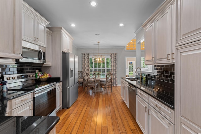kitchen with an inviting chandelier, a sink, light wood-style floors, stainless steel appliances, and decorative backsplash