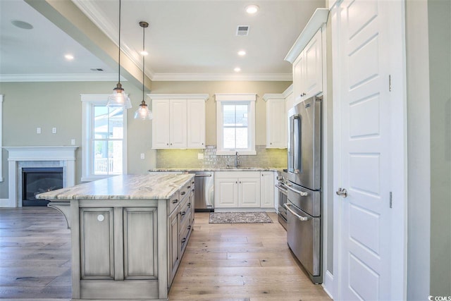 kitchen with appliances with stainless steel finishes, white cabinets, a kitchen island, light stone countertops, and light hardwood / wood-style flooring