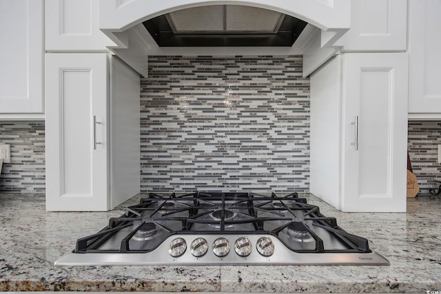 details featuring custom range hood, stainless steel gas stovetop, tasteful backsplash, and white cabinets