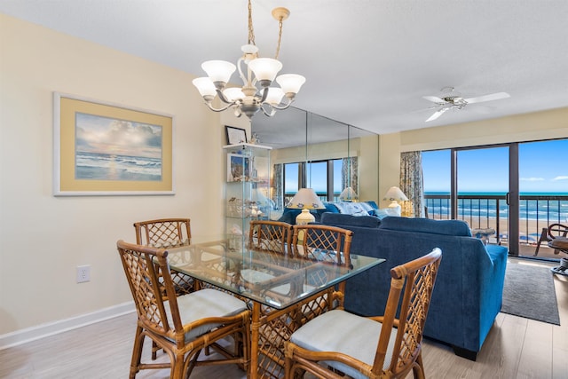 dining space with ceiling fan with notable chandelier, a water view, and light hardwood / wood-style flooring