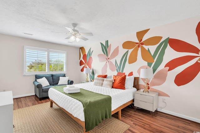 bedroom featuring visible vents, a ceiling fan, a textured ceiling, wood finished floors, and baseboards