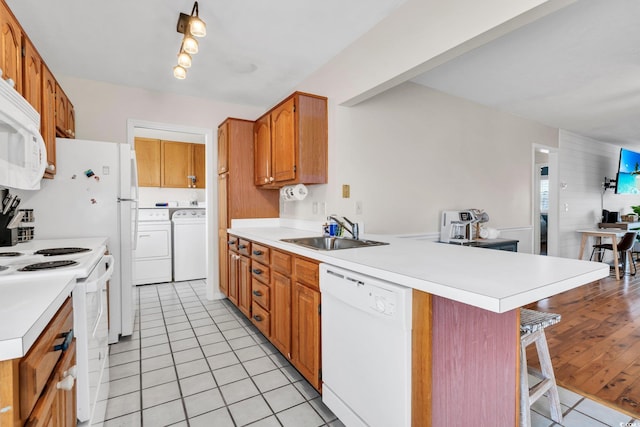 kitchen featuring white appliances, a kitchen breakfast bar, a peninsula, washing machine and dryer, and a sink