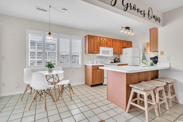 kitchen featuring pendant lighting, white appliances, a kitchen bar, kitchen peninsula, and sink