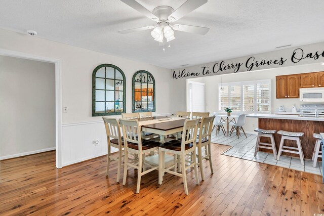 dining area featuring light wood-type flooring, ceiling fan, and a textured ceiling