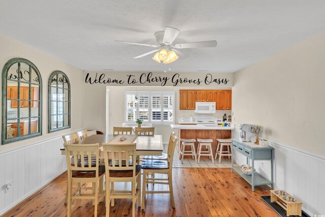 dining area featuring light wood-type flooring, a textured ceiling, and ceiling fan