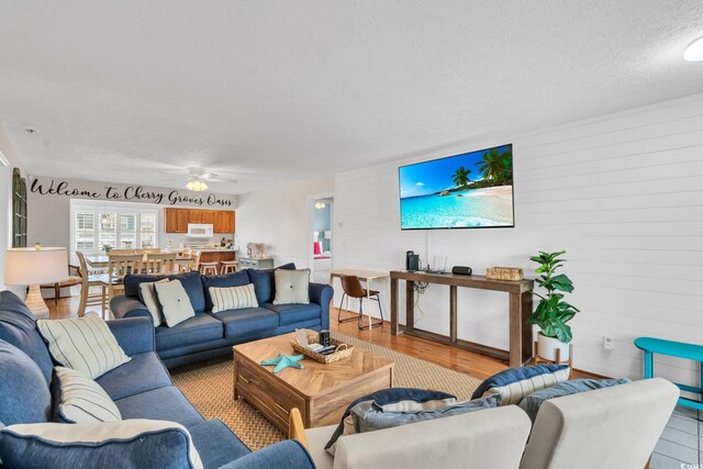 living room featuring a textured ceiling, wooden walls, ceiling fan, and light hardwood / wood-style floors