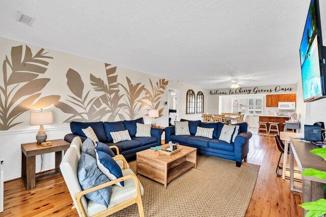 living room with a textured ceiling, light hardwood / wood-style flooring, and ceiling fan