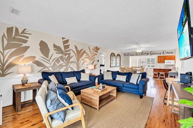 living room featuring a textured ceiling, visible vents, and light wood-style floors