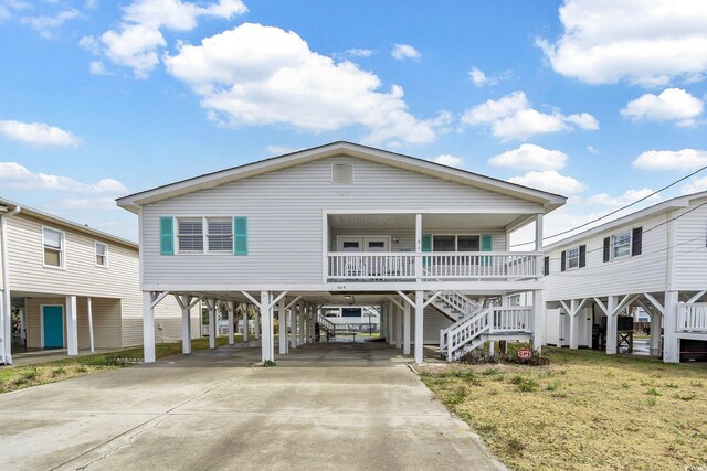 raised beach house with a porch, a carport, and a front lawn