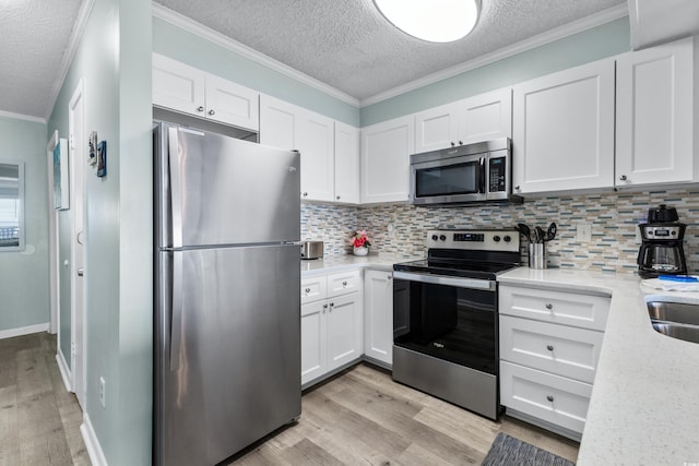 kitchen with light stone counters, white cabinets, stainless steel appliances, light wood-type flooring, and ornamental molding