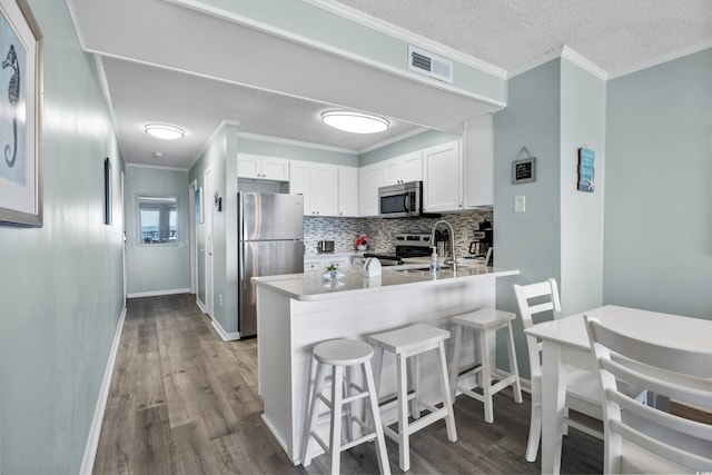 kitchen featuring a breakfast bar, white cabinetry, kitchen peninsula, light hardwood / wood-style flooring, and stainless steel appliances