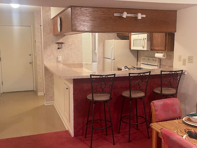 kitchen with white appliances, a breakfast bar area, kitchen peninsula, and carpet floors