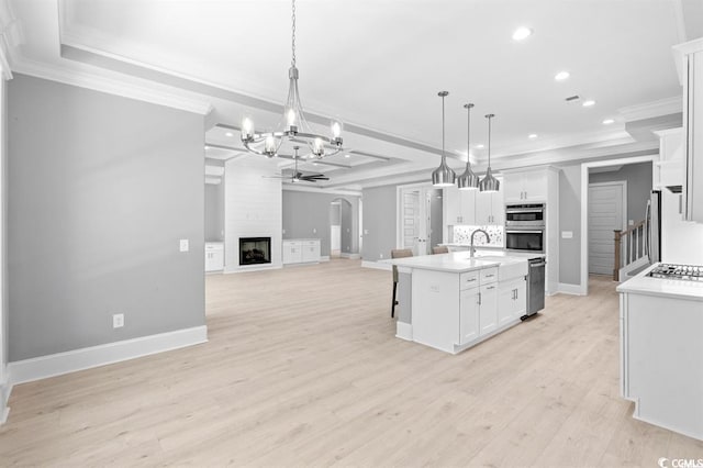 kitchen with a large fireplace, an island with sink, white cabinets, and light hardwood / wood-style flooring