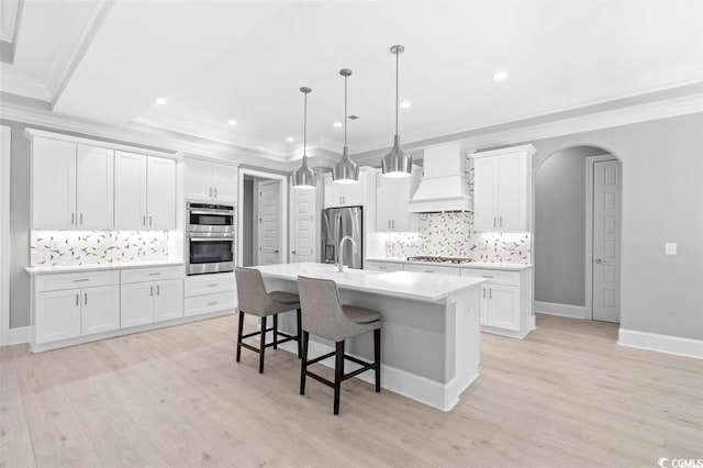 kitchen featuring light wood-type flooring, premium range hood, backsplash, and a kitchen island with sink