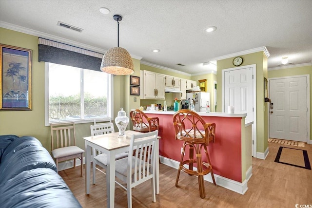 dining space featuring visible vents, crown molding, a textured ceiling, and light wood-type flooring