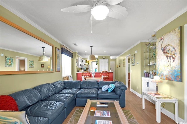 living room featuring visible vents, wood finished floors, crown molding, baseboards, and ceiling fan