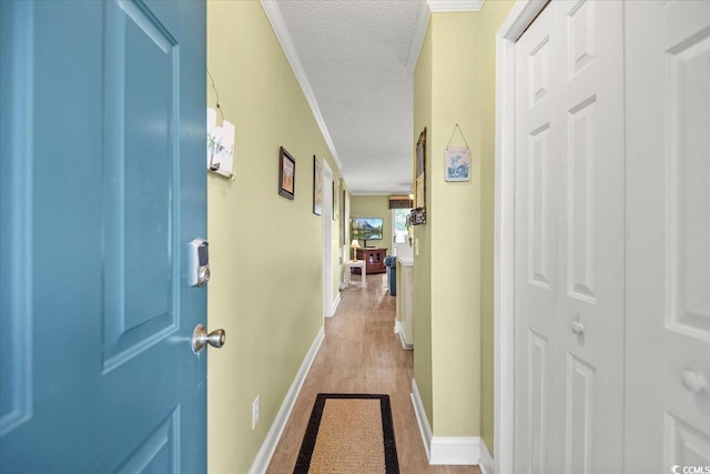 hallway with a textured ceiling, wood finished floors, baseboards, and ornamental molding