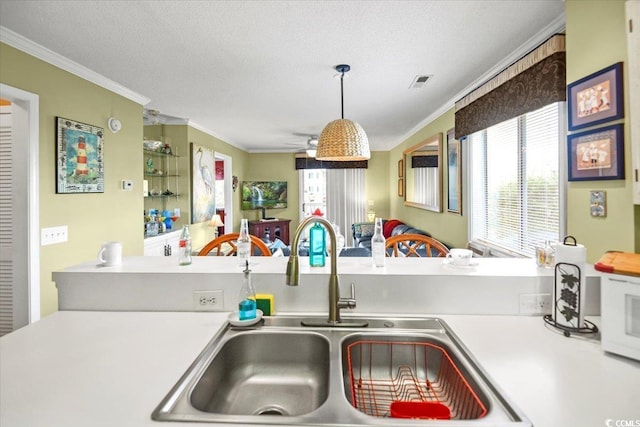 kitchen with white microwave, ornamental molding, light countertops, and a sink