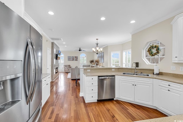 kitchen with stainless steel appliances, a peninsula, a sink, light wood-style floors, and open floor plan