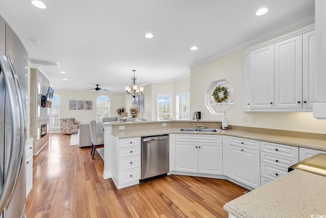 kitchen with light wood-style flooring, a peninsula, a sink, open floor plan, and appliances with stainless steel finishes