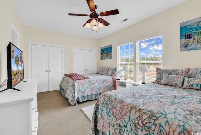 carpeted bedroom featuring two closets, visible vents, and a ceiling fan