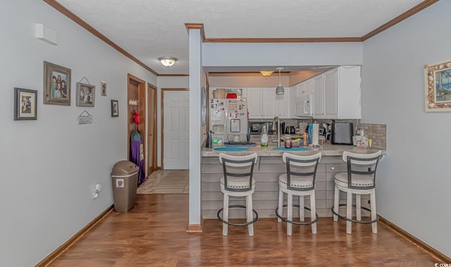 kitchen featuring white appliances, a breakfast bar, ornamental molding, hardwood / wood-style flooring, and white cabinets