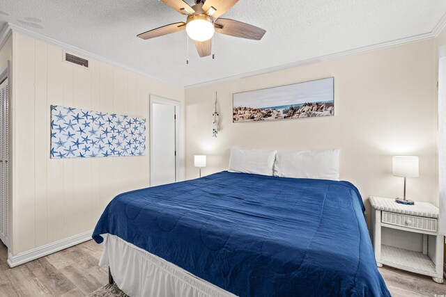 bedroom featuring ceiling fan, light hardwood / wood-style floors, a textured ceiling, and ornamental molding