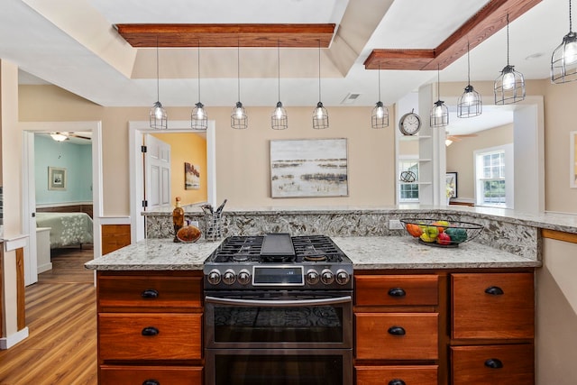 kitchen with decorative light fixtures, ceiling fan, stainless steel gas stove, and light hardwood / wood-style flooring