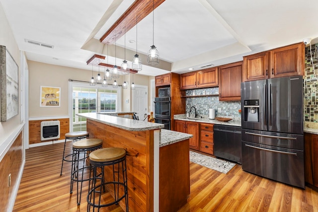 kitchen featuring heating unit, light wood-type flooring, black appliances, pendant lighting, and decorative backsplash