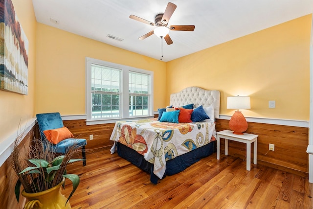 bedroom with ceiling fan, wood walls, and hardwood / wood-style flooring